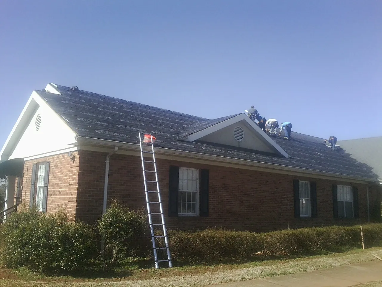 Crew tearing shingles off a brick ranch roof with a ladder set — Metal Roof Repair work by our crew in Hooversville