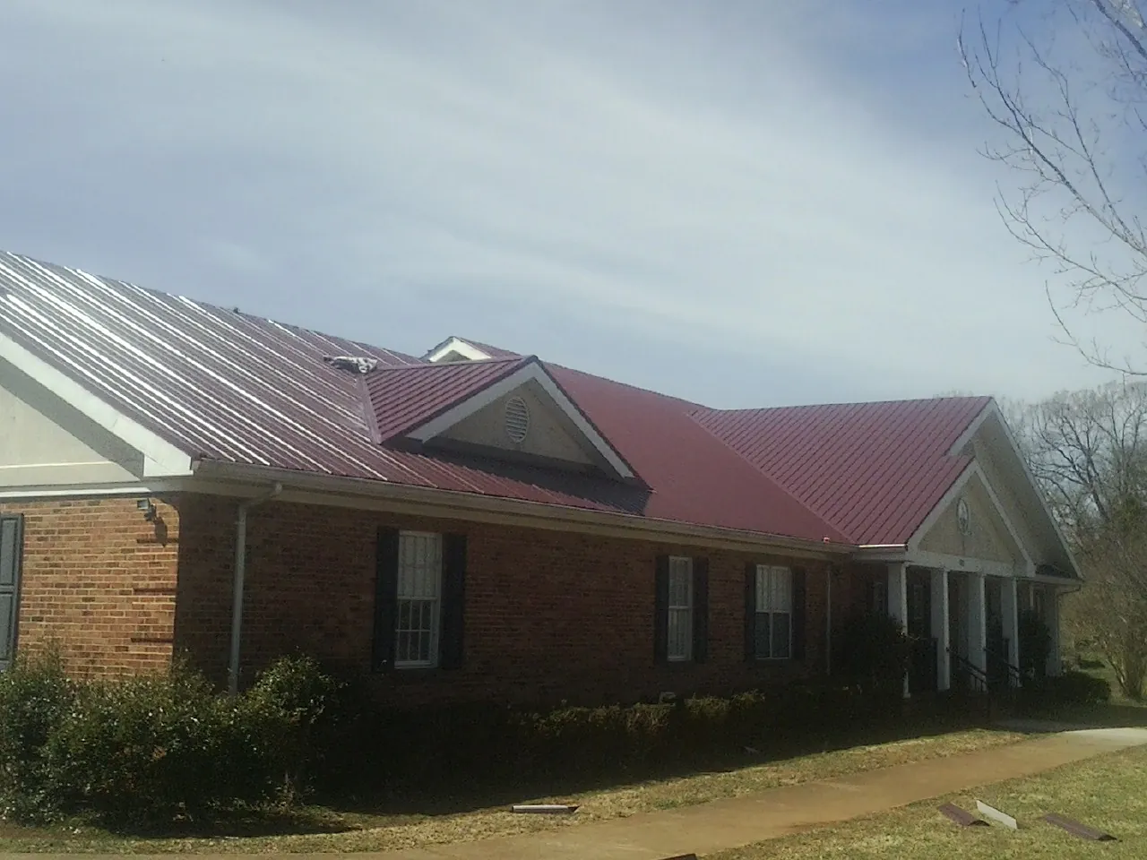 Red metal roof with gabled entries on a long brick building, from a Hail Damage Roof Repair job in Hooversville