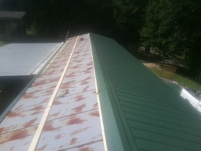 Old rusted panels beside newly installed green metal roofing — Wind Damage Roof Repair by Roofing Brothers in Hooversville