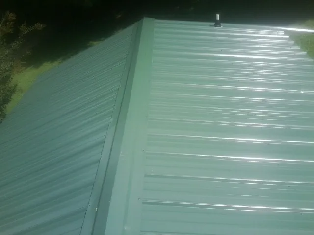 New green metal panels meeting at the ridge of a roof — Flat Roof Repair work by our crew in Hooversville