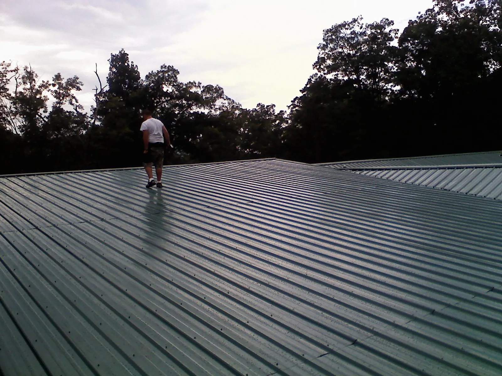 Roofer walking a wide expanse of new green metal roofing in Hooversville