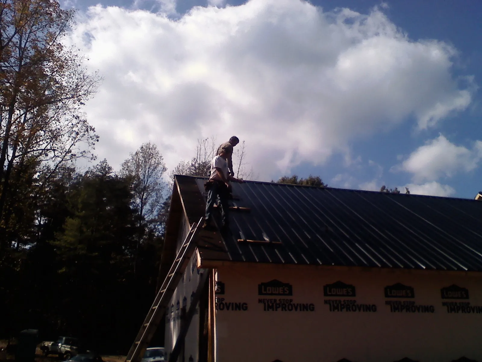 Roofer fastening dark metal panels high against a cloudy sky, from a Roof Inspection job in Hooversville