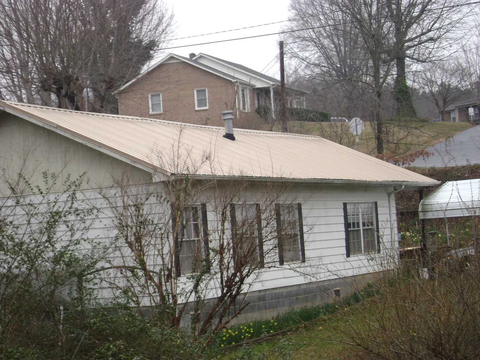 Tan metal roof on a white sided house set into a hillside — Commercial Roofing by Roofing Brothers in Hooversville